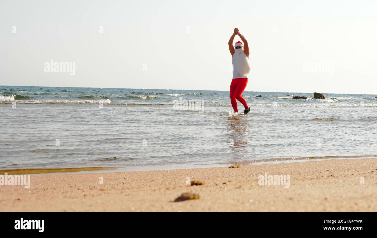 Babbo Natale divertente. Babbo Natale, in occhiali da sole e pinne, divertendosi nell'acqua di mare vicino alla spiaggia sabbiosa. Vacanze estive a Babbo Natale. Foto di alta qualità Foto Stock