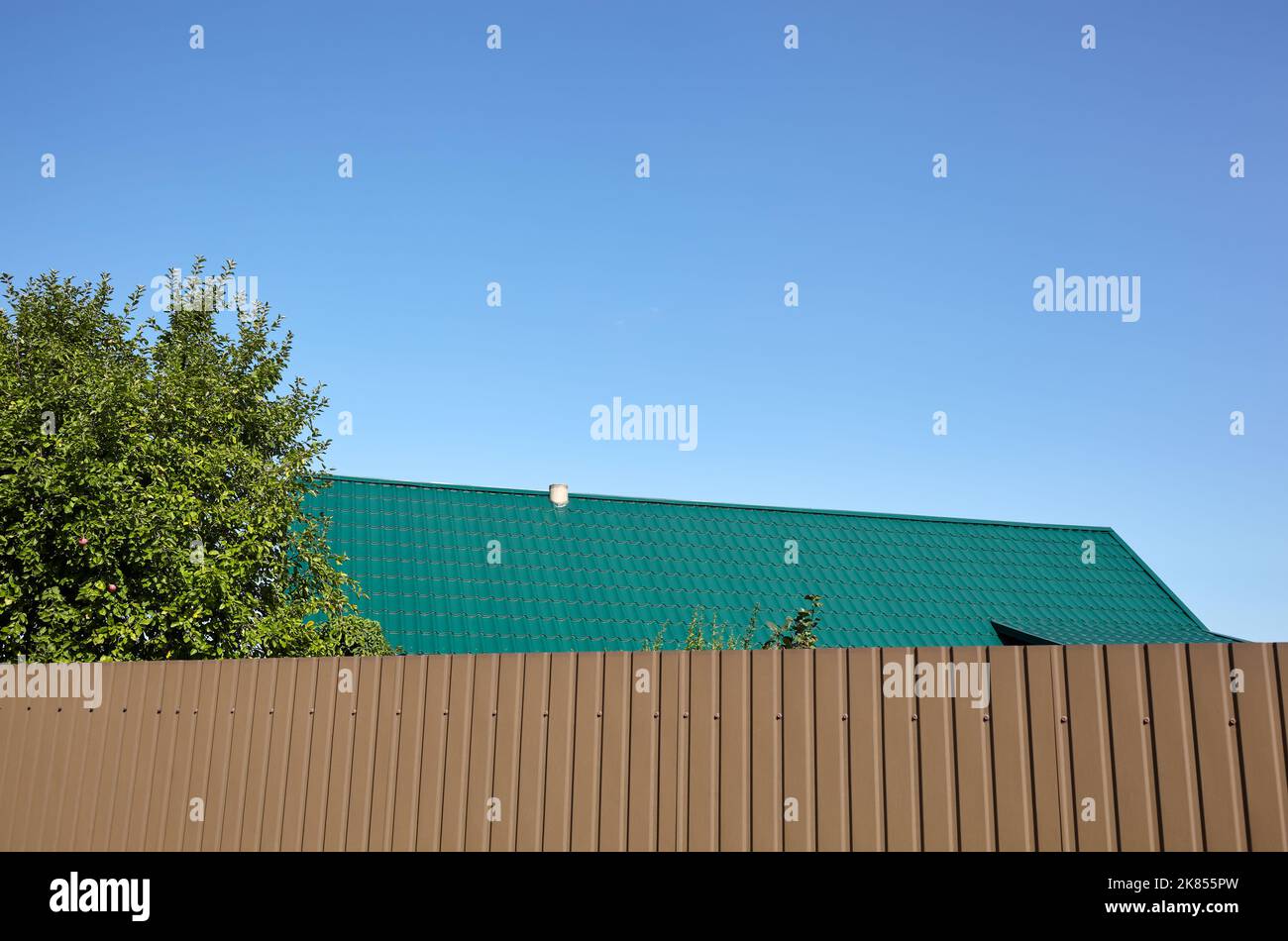 Tetto della casa sullo sfondo di una recinzione metallica. Piastrelle di metallo contro il cielo blu Foto Stock