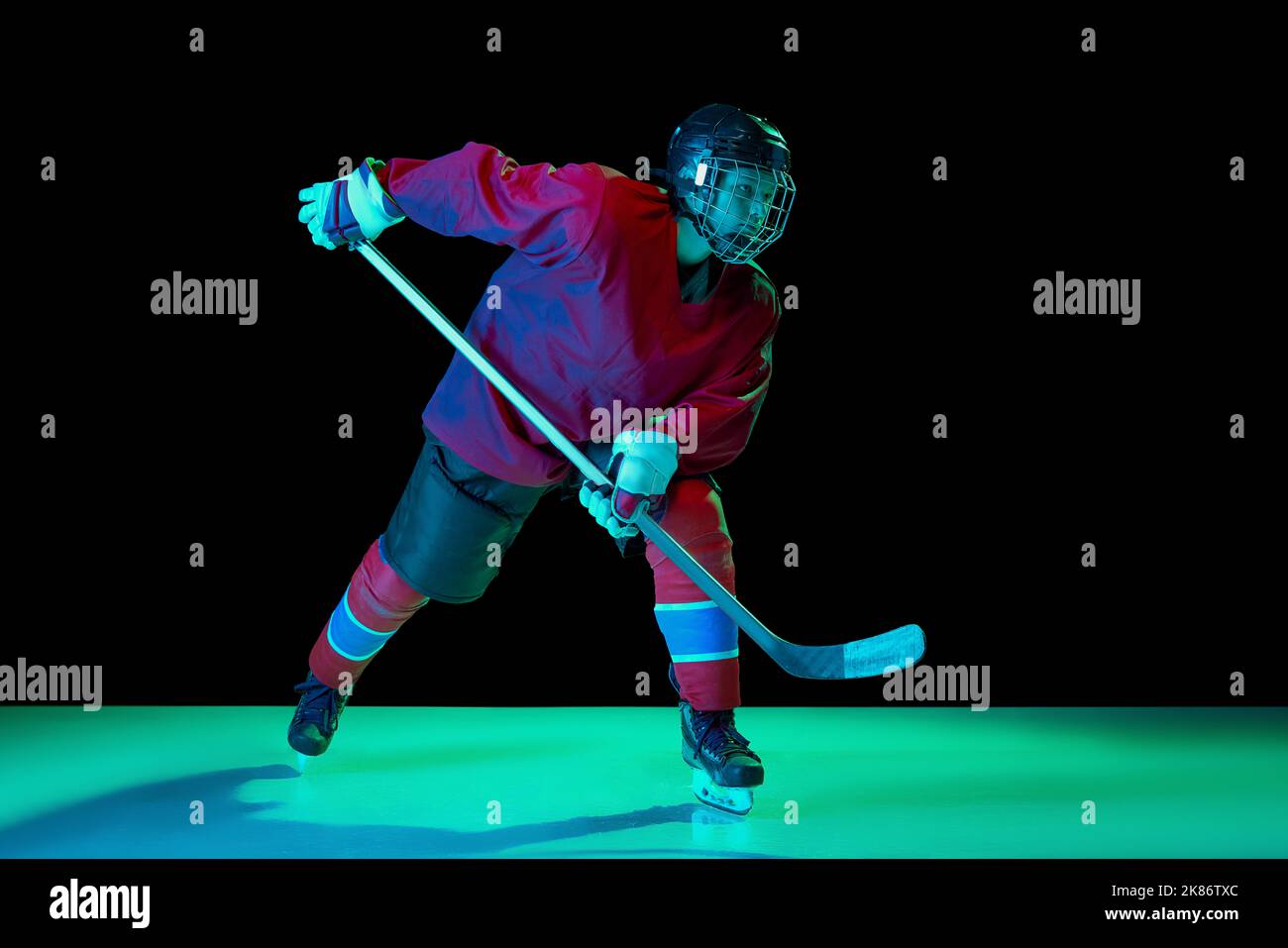 Allenamento di un giocatore di hockey su ghiaccio maschile che indossa maglia da hockey, uniforme e casco sportivo in movimento isolato su sfondo scuro in luce al neon Foto Stock