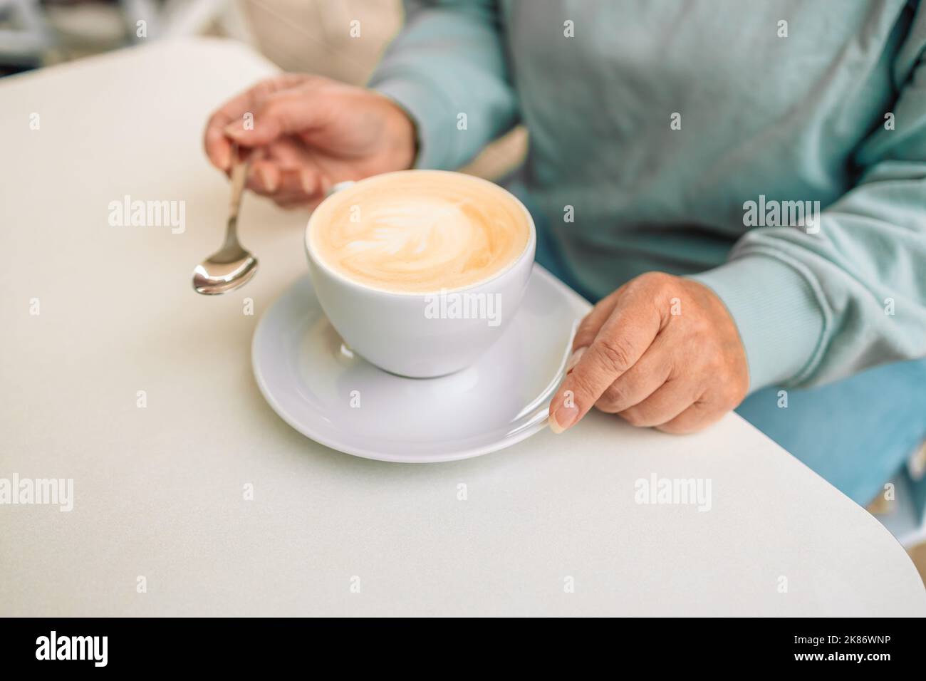 Le mani femminili tengono una tazza di ceramica di fragrante latte o cappuccino su un tavolo in un accogliente caffè della città Foto Stock