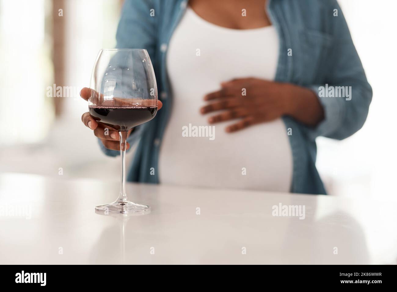 L'alcool può causare problemi per lo sviluppo del vostro bambino. Primo piano di una donna incinta che tiene a casa un bicchiere di vino rosso. Foto Stock