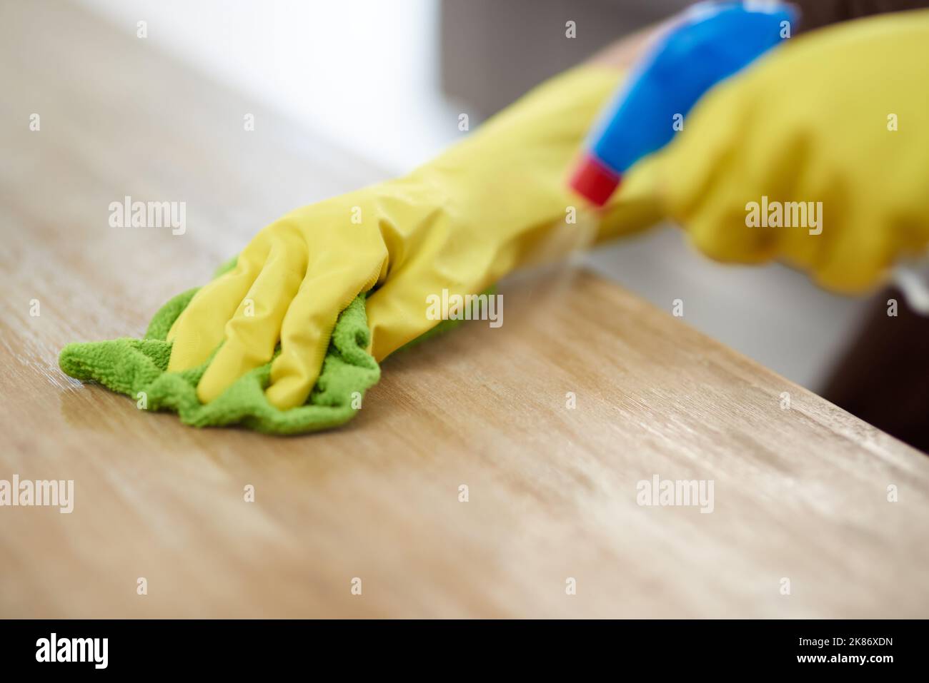 Non si sa mai dove il germe potrebbe essere in agguato. Una donna che indossa i guanti e tiene un flacone spray mentre pulisce una superficie di legno a casa. Foto Stock