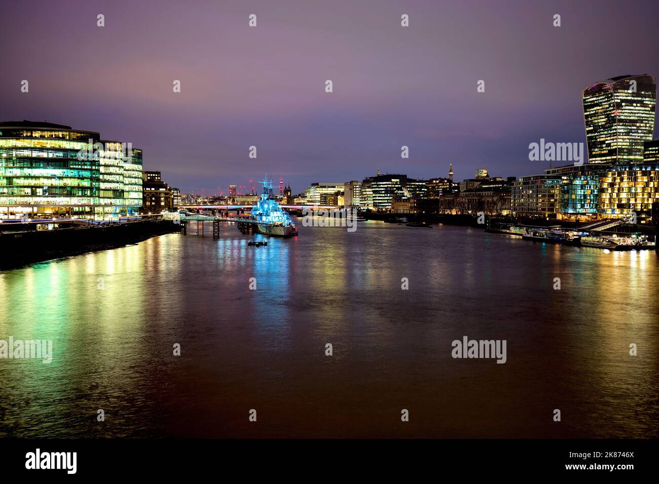 L'HMS Belfast City-class Light Cruiser illuminata di notte con edifici residenziali sul fiume Foto Stock