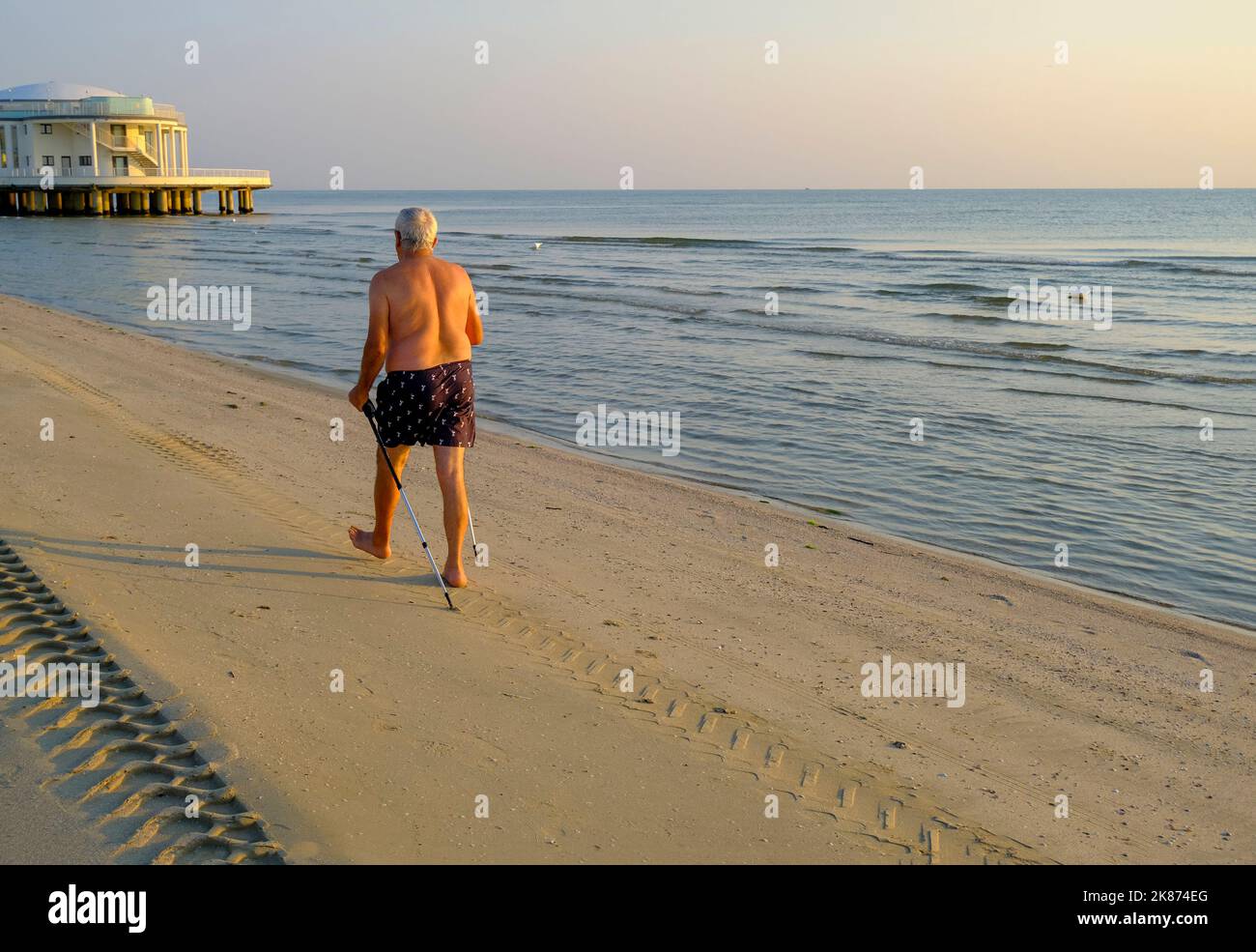 Luglio 2022 Senigallia, Italia: Uomo anziano che cammina con un bastone verso rotonda al mare sulla spiaggia attraverso il mare, il cielo all'alba e l'orizzonte Foto Stock