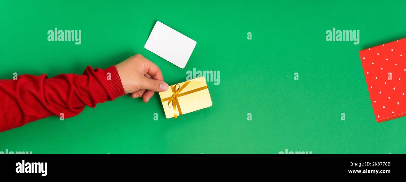 Modello di carta regalo e bonus con un arco in mani femminili su un concetto di sfondo verde di preparazione e acquisto di regali per Natale e Capodanno Banner Foto Stock