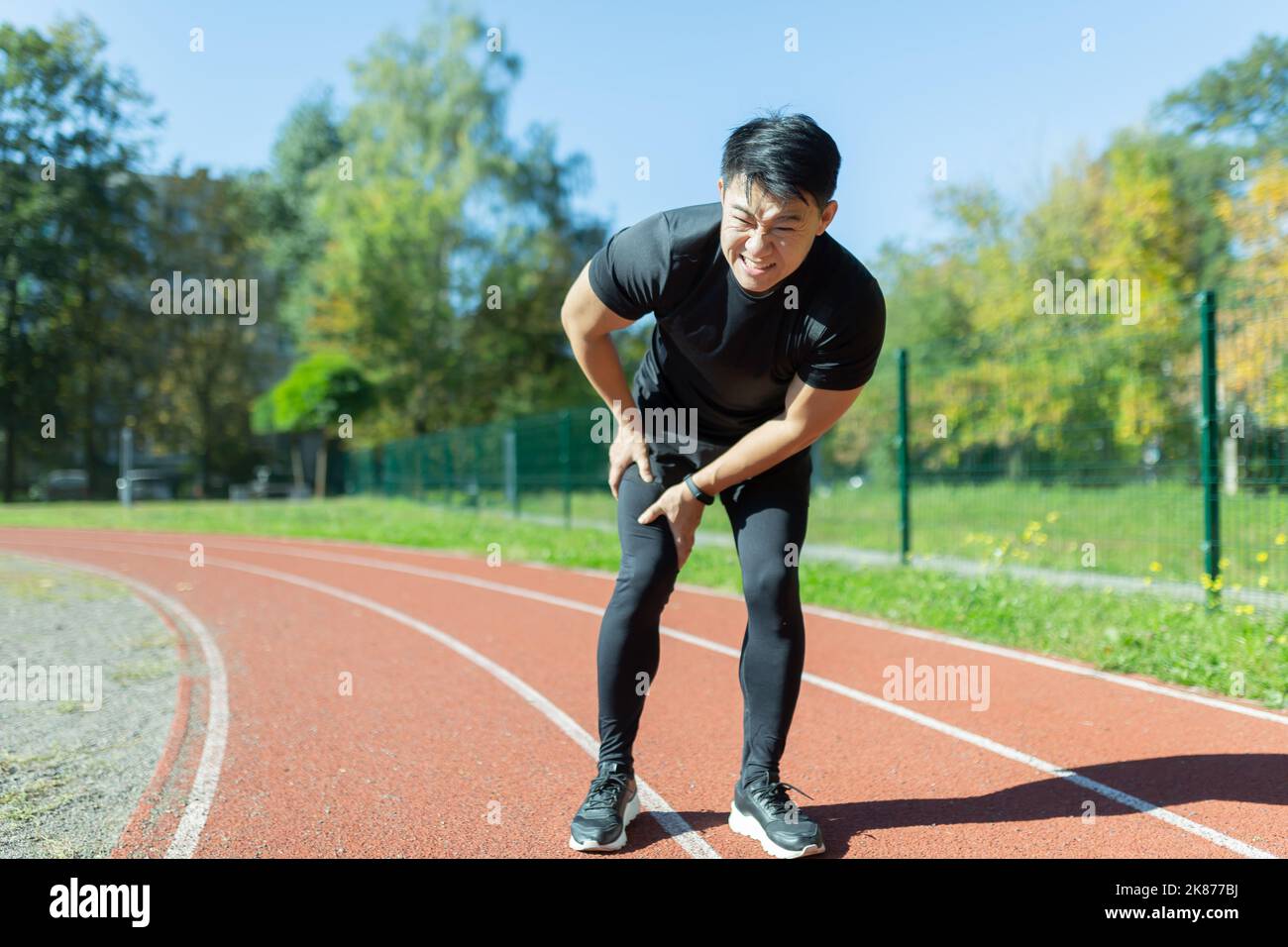 giovane atleta asiatico con dolore muscolare. Uomo che massaggia stretching, trauma lesioni mentre jogging allo stadio all'aperto. Fitness maschio Sprrain dolore grave stretch tirare. Gamba muscolo crampi sport di vitello Foto Stock