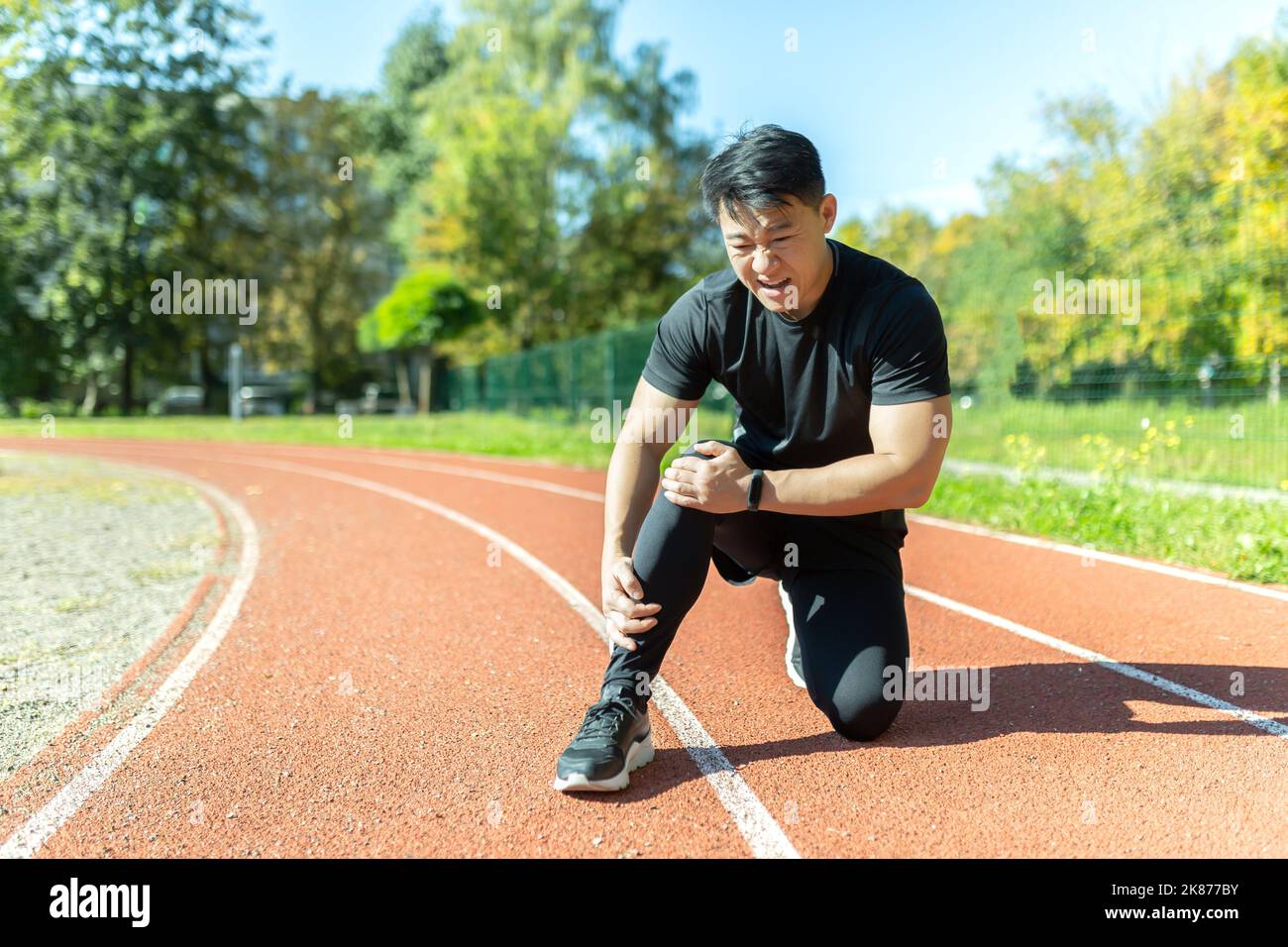L'uomo asiatico dopo allenamento e jogging si siede a terra e soffre di dolori alle gambe, massaggia i muscoli delle gambe Foto Stock