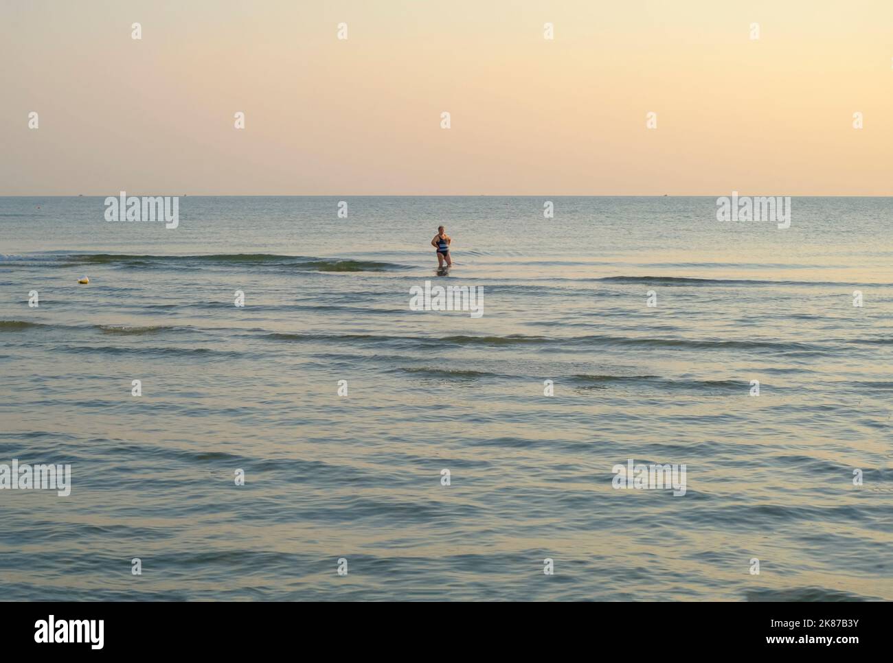 Luglio 2022 Senigallia, Italia: Donna anziana che cammina in mare al tramonto acros l'orizzonte. Foto Stock