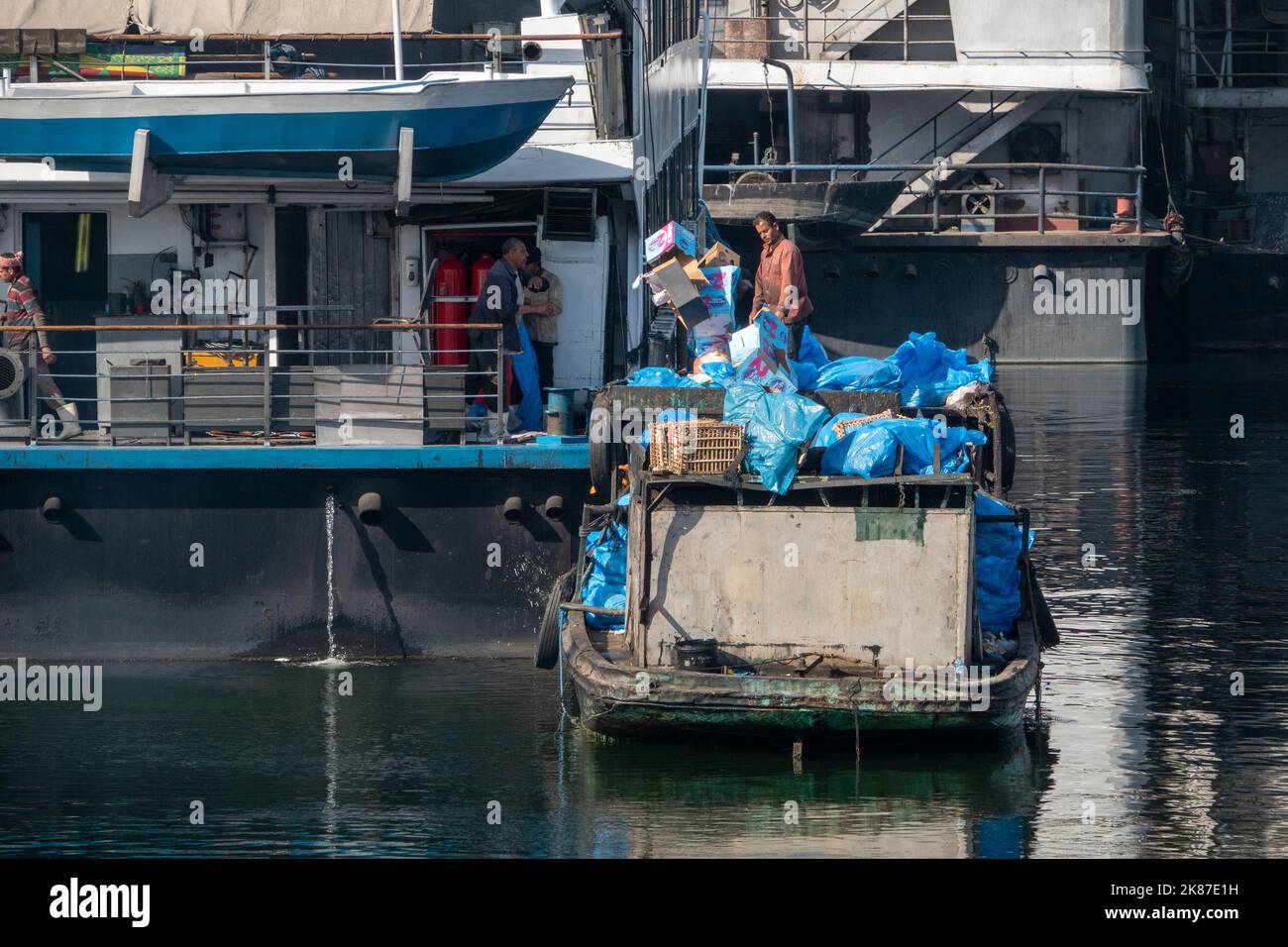 Una chiatta per lo smaltimento dei rifiuti per le navi da crociera sul Nilo con uomini che scaricano borse blu Foto Stock
