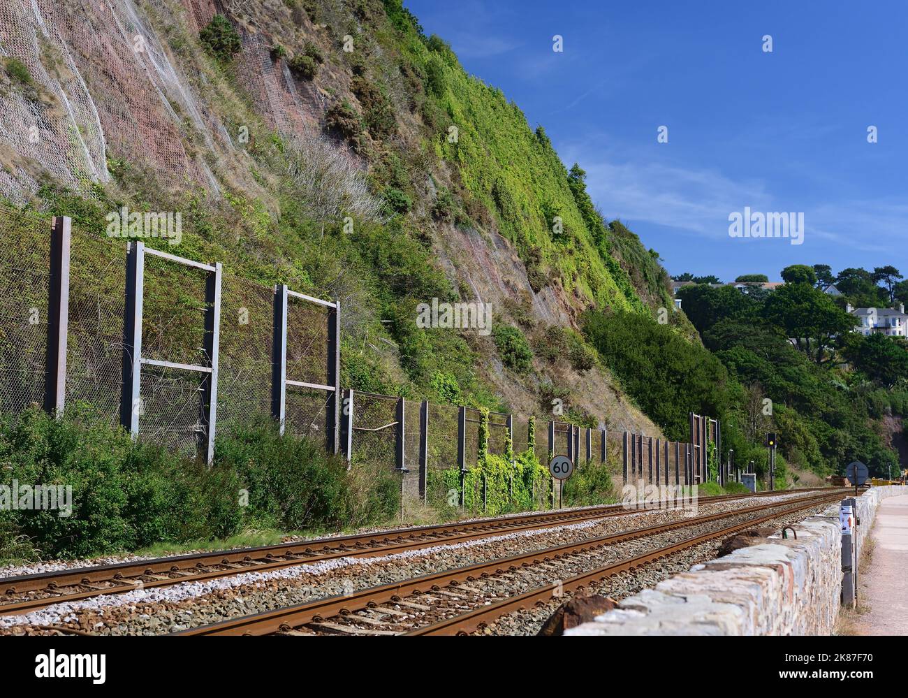 Un cielo blu profondo sopra le scogliere di arenaria rossa e una recinzione che protegge la linea ferroviaria costiera dalle rocce che cadono. Fotografato con un filtro polarizzante. Foto Stock