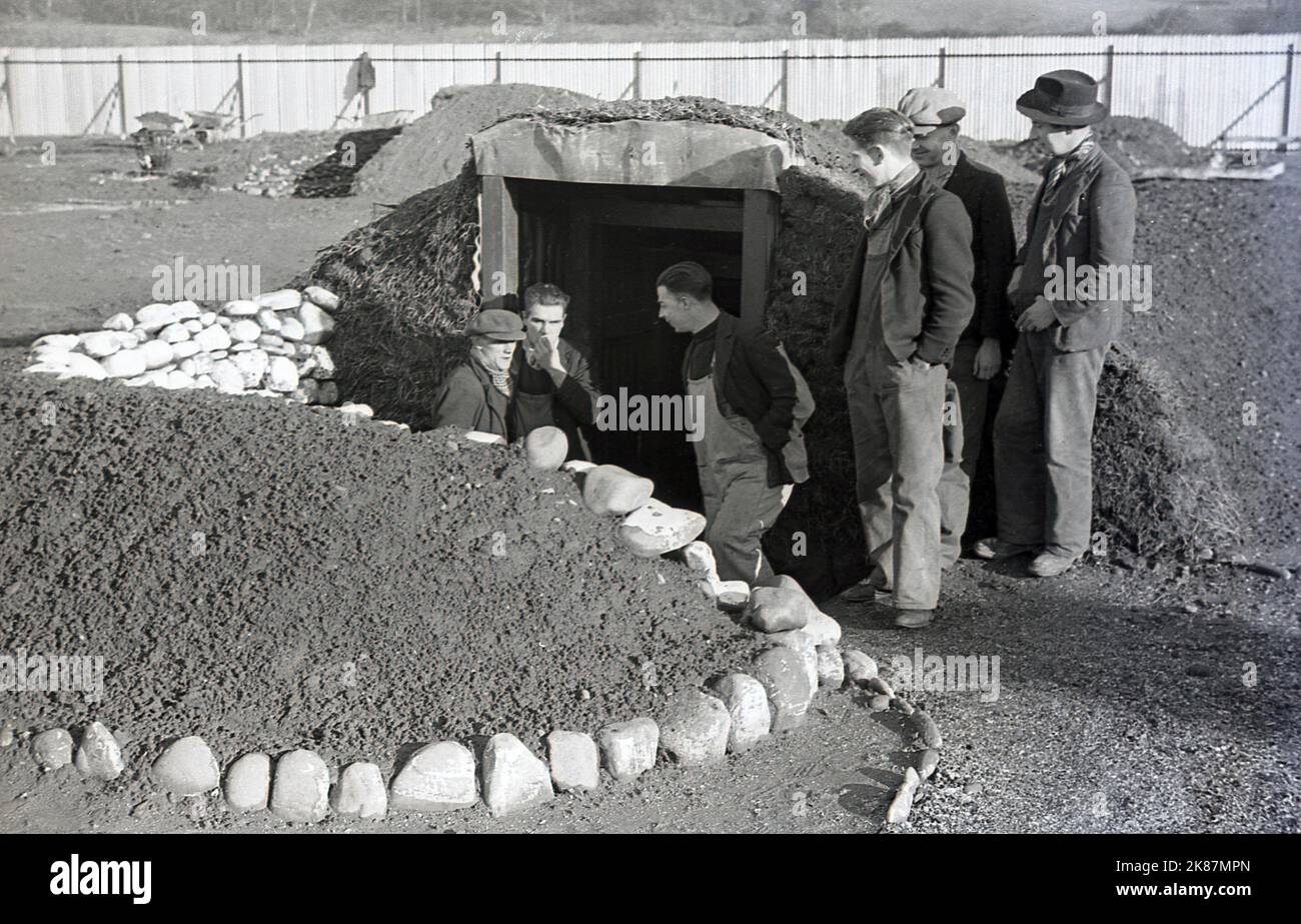 1938, storici, lavoratori gallesi all'ingresso di un rifugio di raid aereo costruito di recente presso la Treforest Industrial Estate, Rhondda, Galles del Sud. Conosciuti anche come rifugi Anderson, dopo l'allora ministro della sicurezza domestica, Sir John Anderson, furono una forma di protezione contro le incursioni aeree nel WW2, essendo strutture in acciaio sepolte a metà strada nel terreno e coperte da uno strato di terra spessa. La loro costruzione iniziò nel 1938 come una mossa preventiva, quando la guerra era all'orizzonte e gli attacchi aerei erano inevitabili. Quando la guerra fu dichiarata nel settembre del 1939, erano stati costruiti circa 1,5 milioni di rifugi. Foto Stock