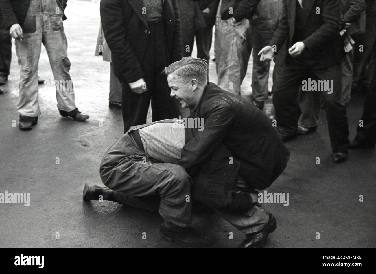 1938, storici, i lavoratori di una zona industriale si riunirono fuori in una pausa, godendo di un po' di aria fresca e frizzosa lontano dal loro lavoro, Treforest, Galles del Sud. Regno Unito, due di loro hanno una finta gara di wrestling! Foto Stock