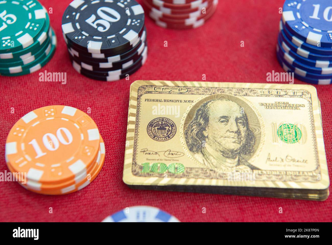 Vista dall'alto delle carte da gioco dorate da 100 dollari accanto alle pile di fiches sul tavolo in feltro rosso. Il gioco di poker è uno dei giochi di carte più popolari al mondo A. Foto Stock