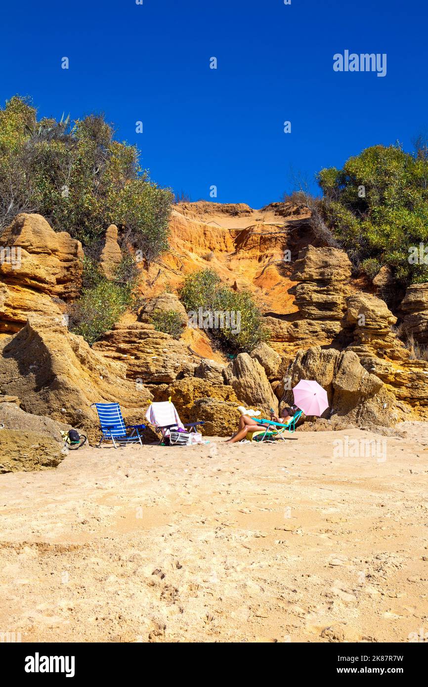 Donna che guarda il telefono, prendere il sole su una sedia a sdraio Playa Sancti Petri spiaggia, Costa de la Luz, Cadice, Spagna Foto Stock