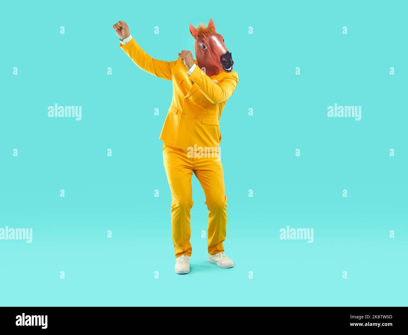 Divertente showman in tuta gialla e maschera di cavallo rosa in gomma che ballano su sfondo turchese. Foto Stock