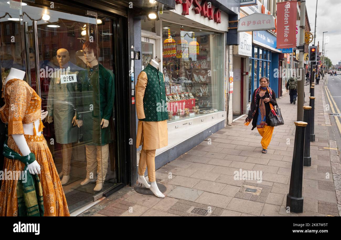 Una donna cammina accanto a un negozio che vende saris e abiti tradizionali del Sud asiatico a Belgrave Road, Leicester. Foto Stock