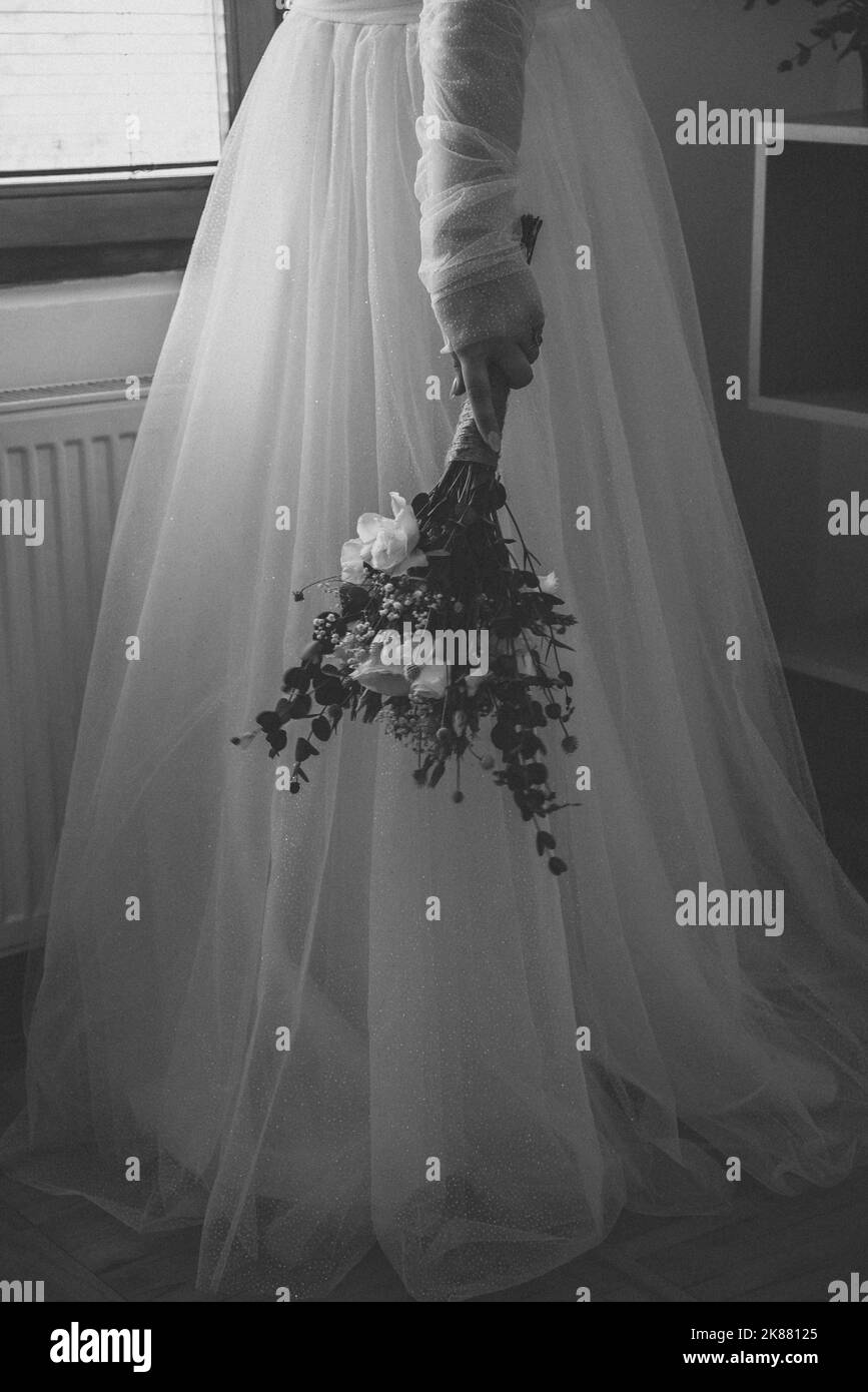 Un colpo in scala di grigi di una sposa che tiene un bouqet di fiori Foto Stock