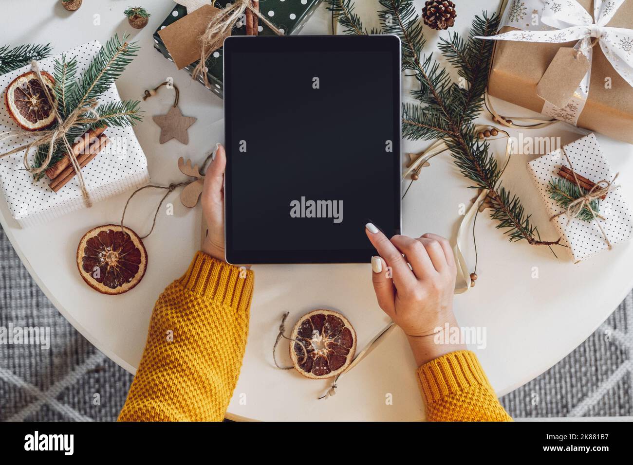 Mani femminili con tablet sul tavolo con decorazioni natalizie fatte a mano Foto Stock