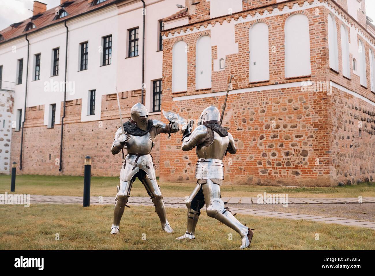 due cavalieri in antiche armature metalliche sono in piedi al muro di pietra del castello combattendo con le spade Foto Stock