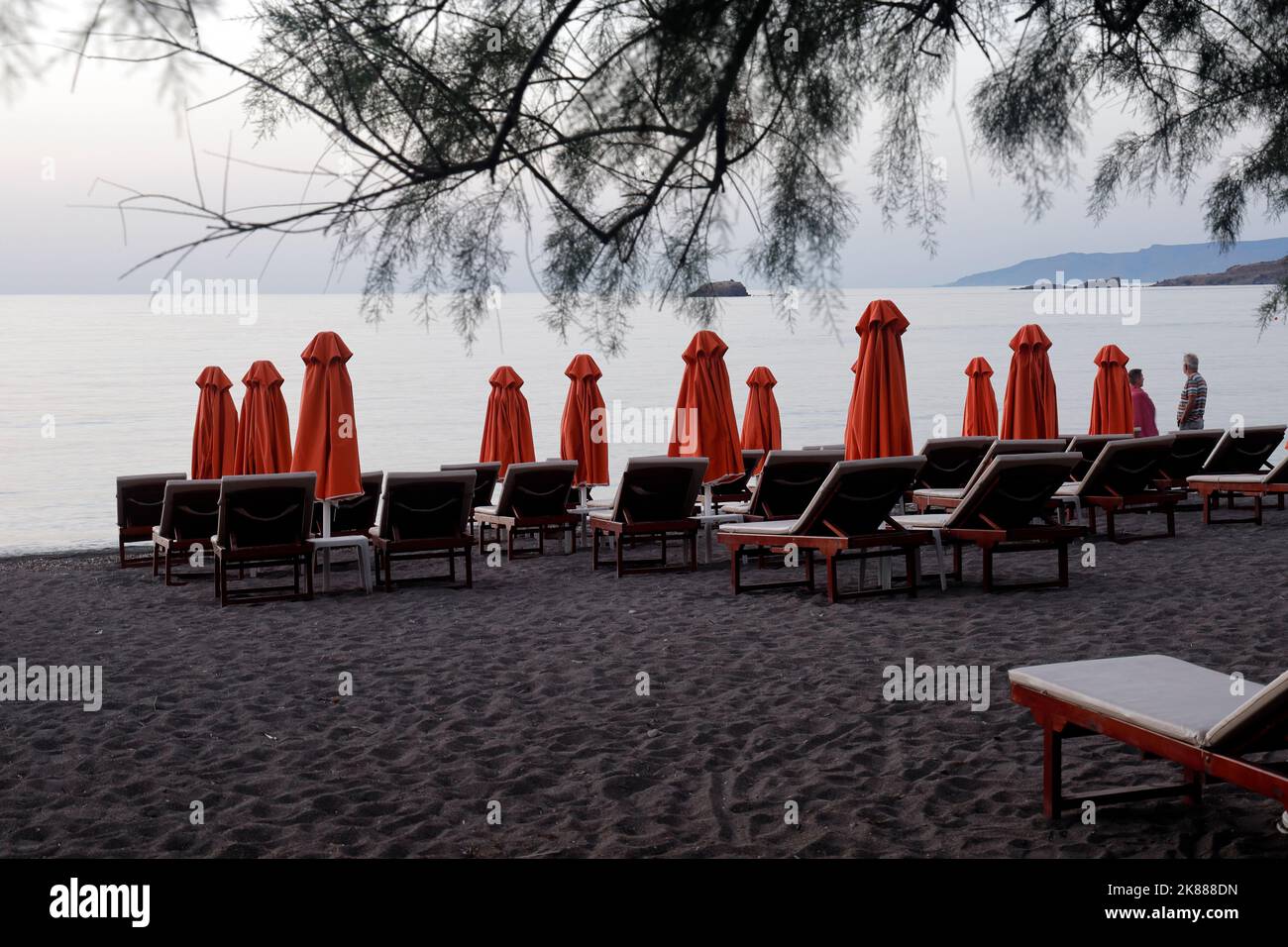 Ombrelloni e sedie a sdraio arancioni, lettini sulla spiaggia, due persone guardano il tramonto. Lesbo. Settembre / Ottobre 2022. Autunno. Foto Stock