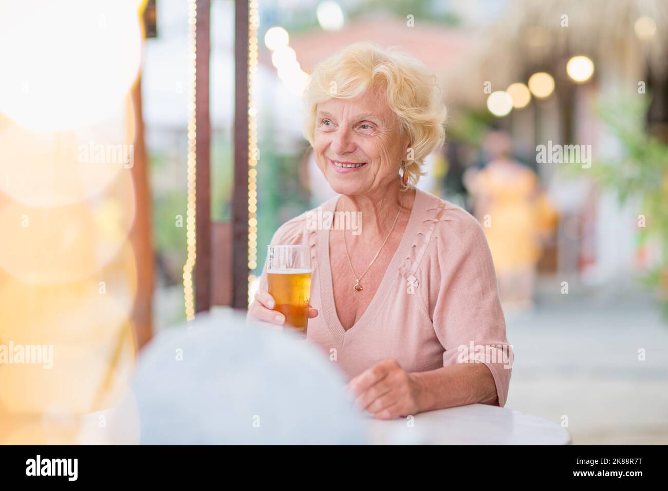 Donna matura seduta a un tavolo in un bar estivo e bere birra Foto Stock