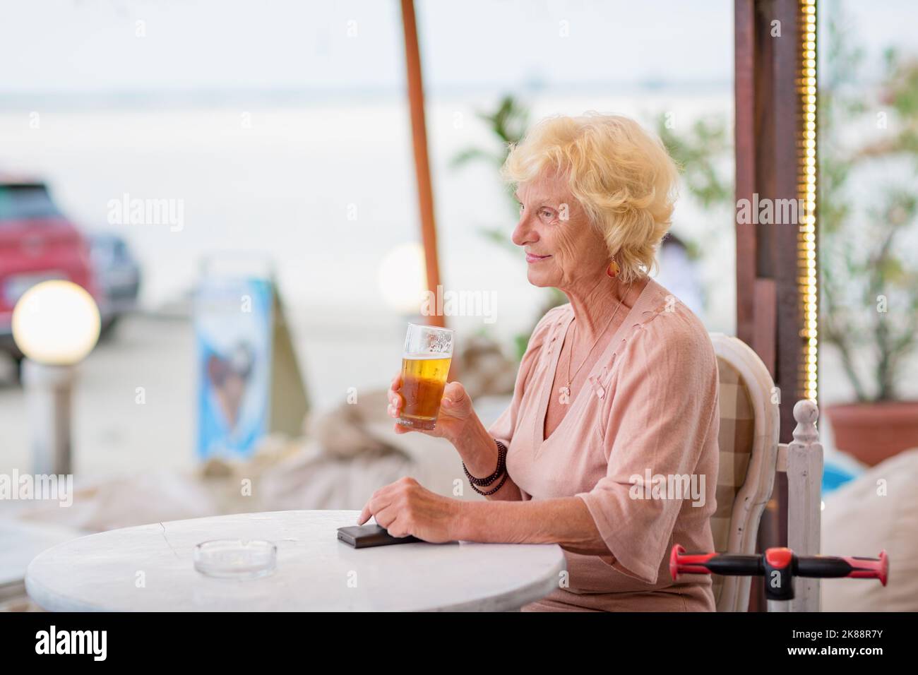 Donna matura seduta a un tavolo in un bar estivo e bere birra Foto Stock