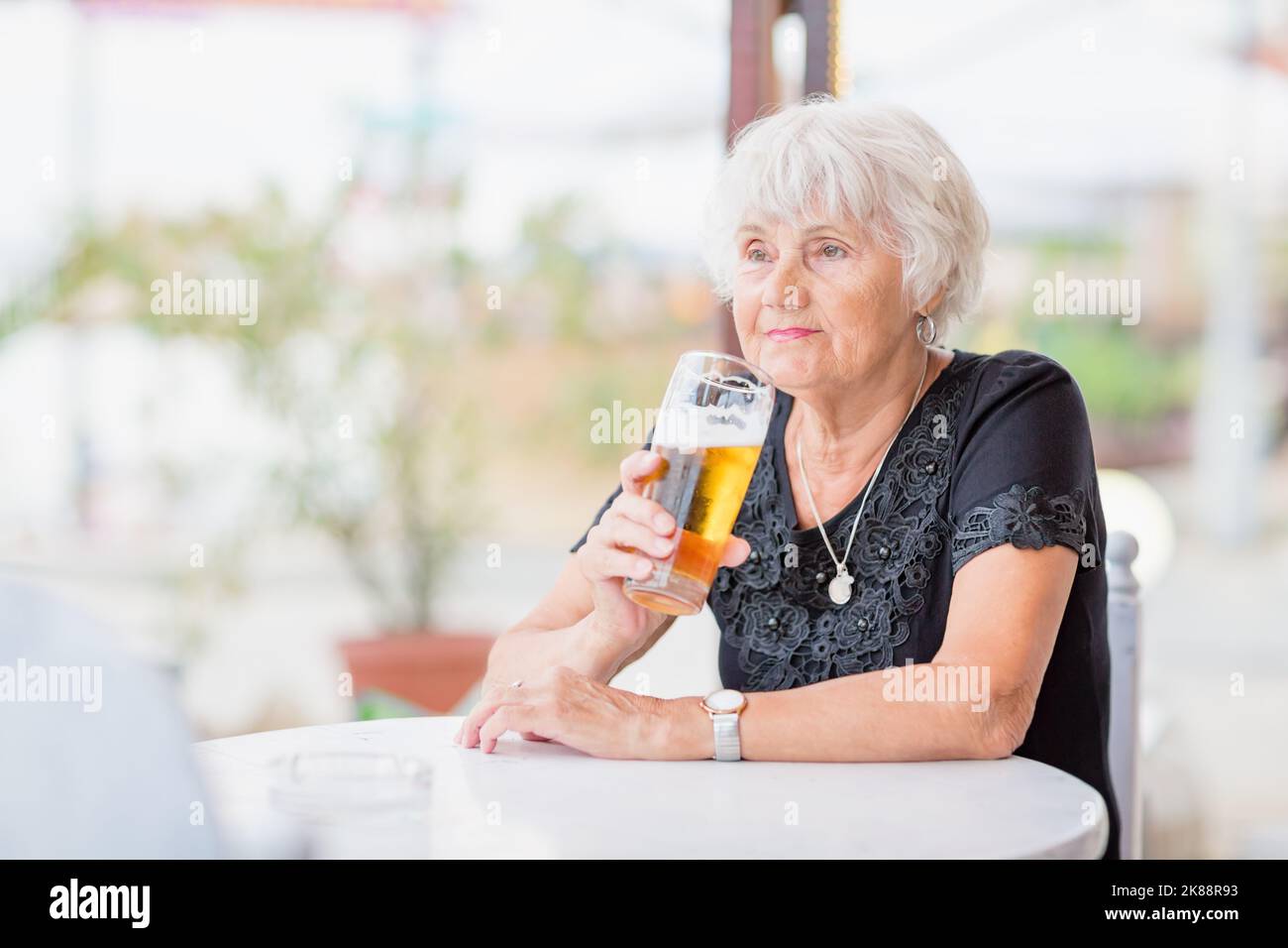 Donna matura seduta a un tavolo in un bar estivo e bere birra Foto Stock