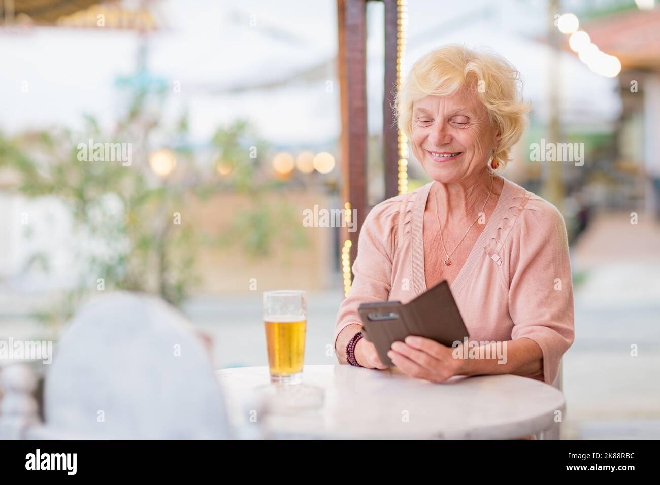 Donna matura seduta a un tavolo in un bar estivo e bere birra Foto Stock