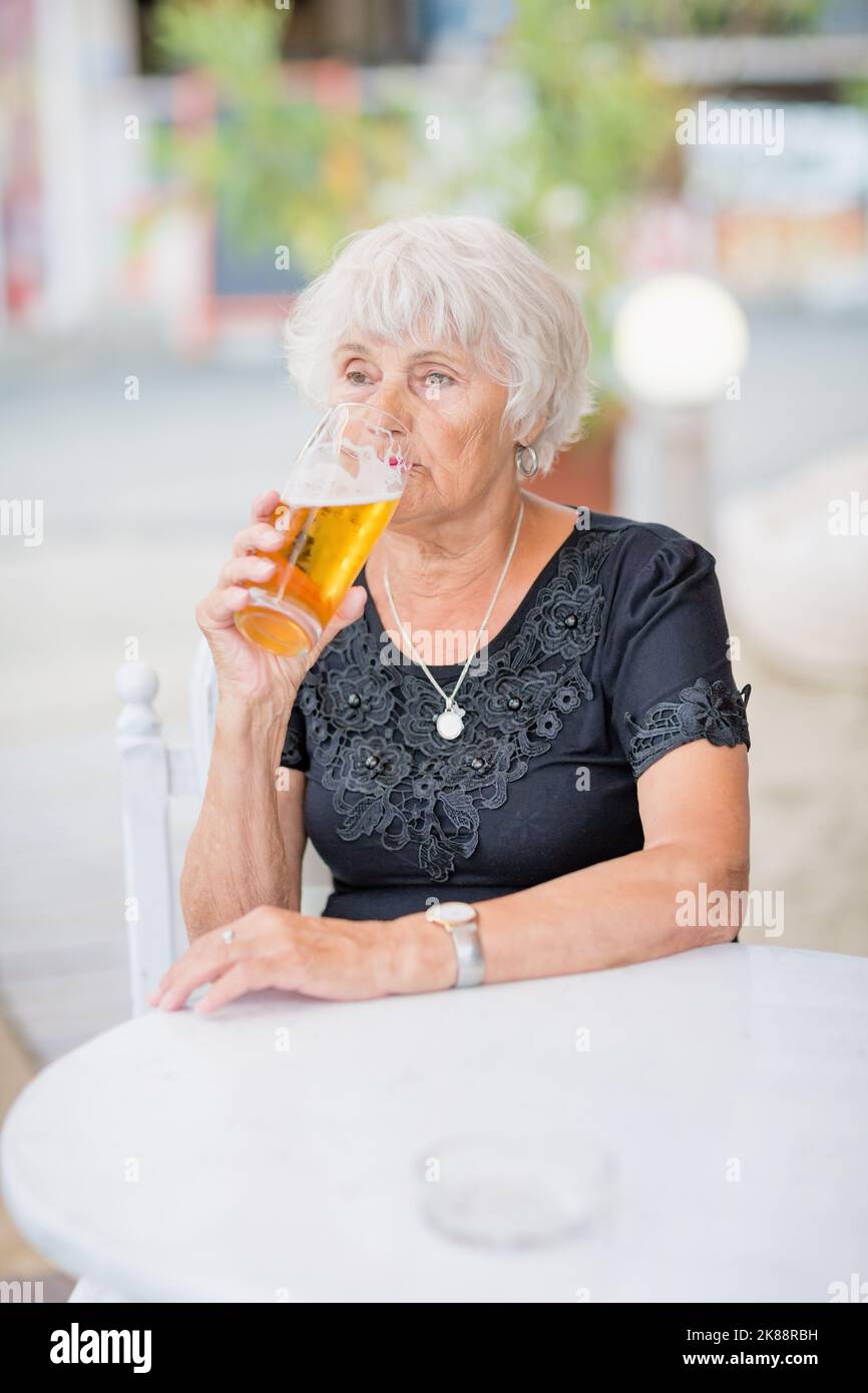Donna matura seduta a un tavolo in un bar estivo e bere birra Foto Stock