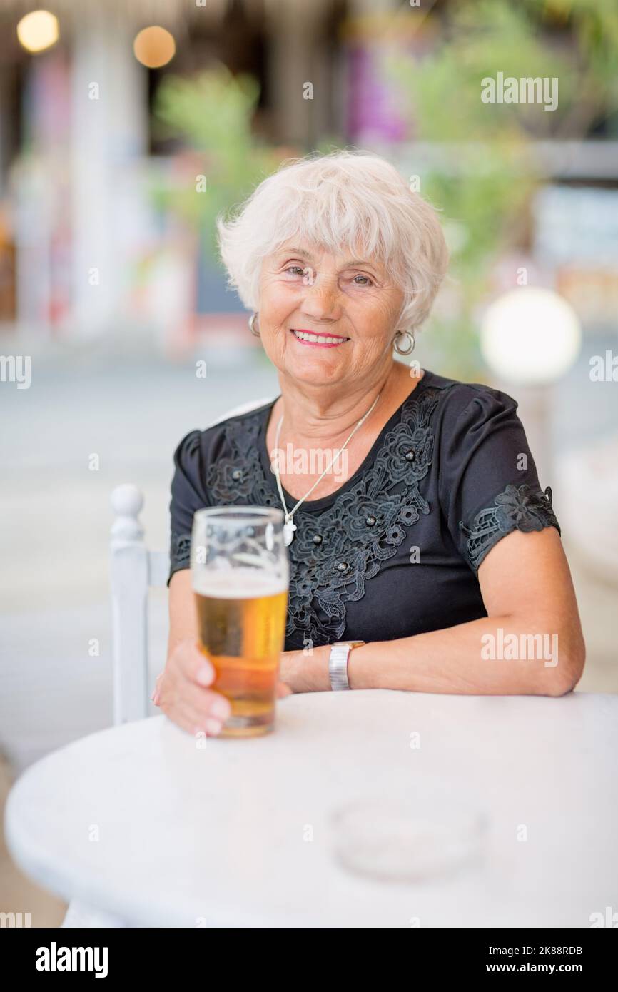Donna matura seduta a un tavolo in un bar estivo e bere birra Foto Stock