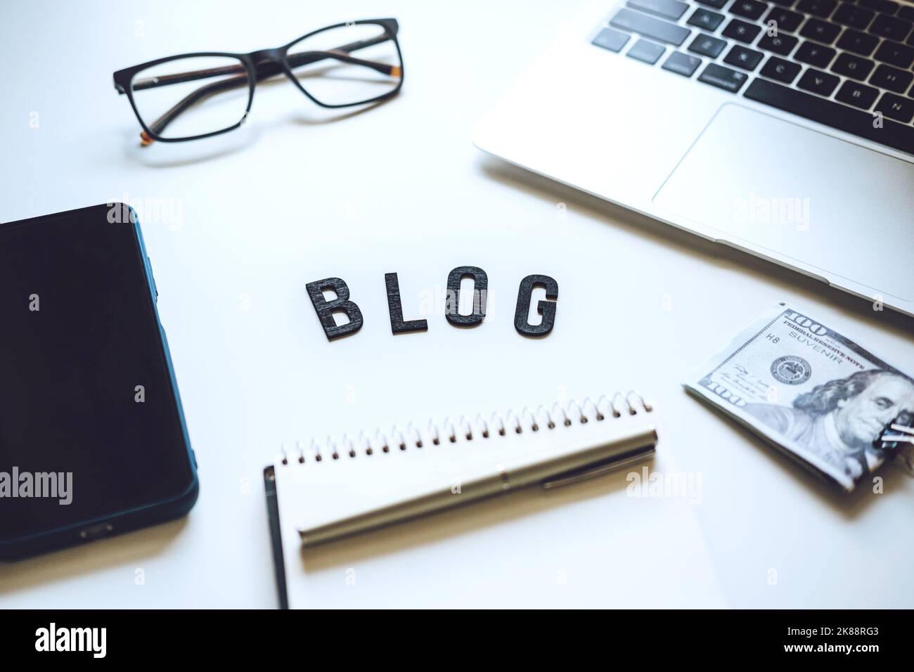 Come iniziare Blog, Blogging per i principianti. Modi per monetizzare il tuo blog. Blog parola sul tavolo con computer portatile, smartphone, notebook aperto, banconote in dollari e. Foto Stock