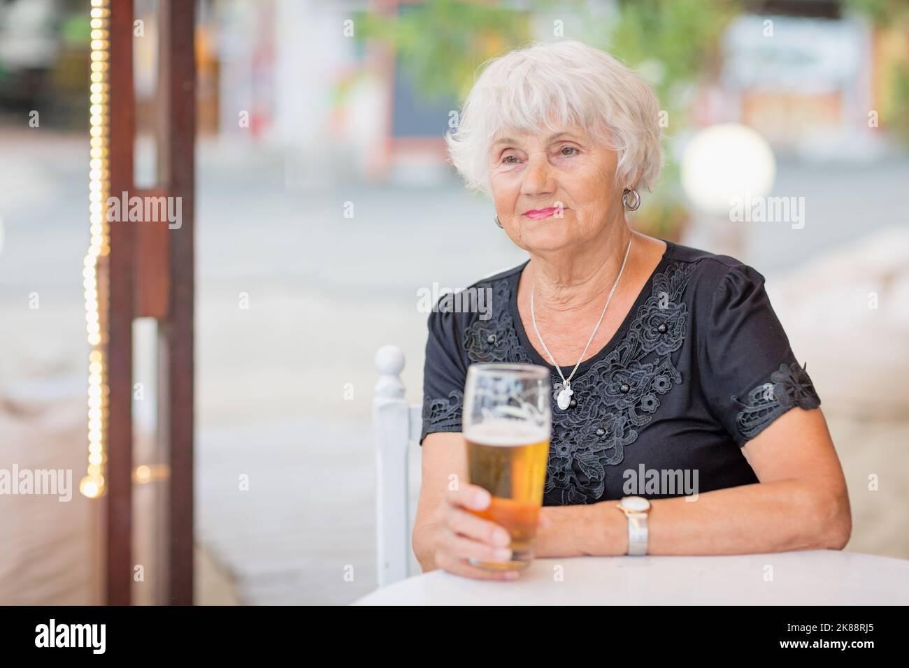 Donna matura seduta a un tavolo in un bar estivo e bere birra Foto Stock