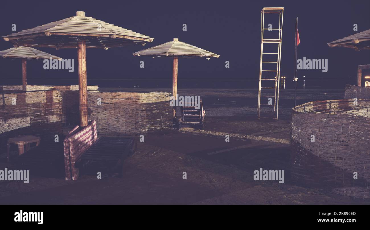 Ombrelloni, lettini e parabrezza in legno su una spiaggia di notte, con applicazione di tonalità cromatiche. Foto Stock