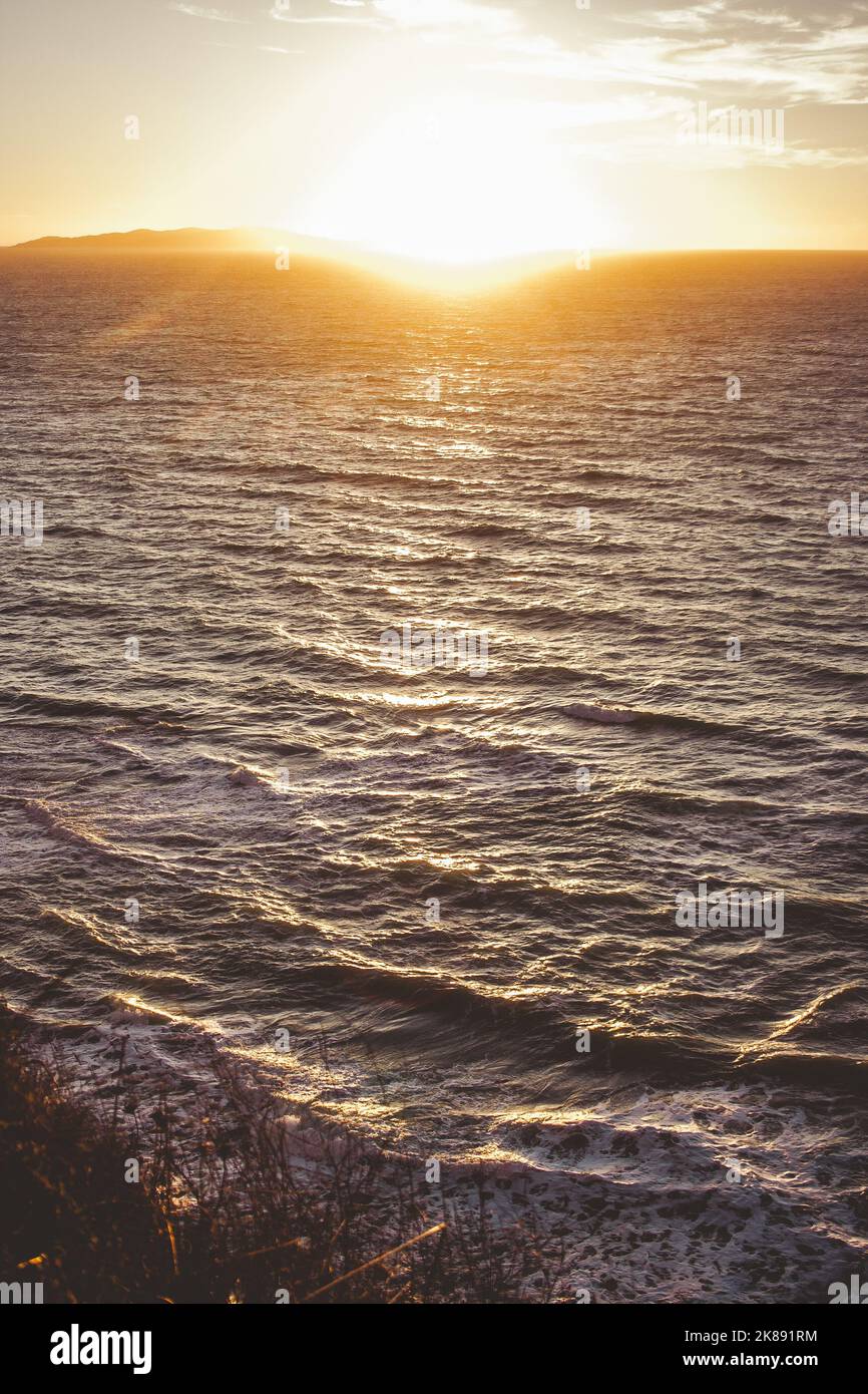 Bellissimo tramonto di acqua ondulata sulla riva del mare in Grecia con le montagne in lontananza. Foto Stock
