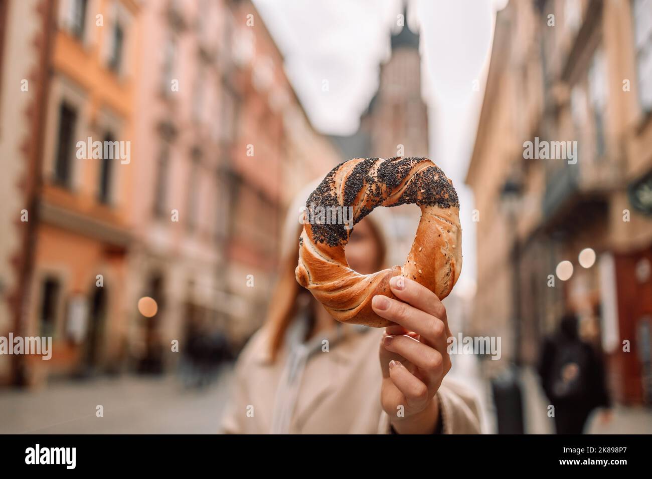 Turista donna che tiene bagel obwarzanek, tradizionale cucina polacca prezel snack sulla piazza del mercato di Cracovia. Foto Stock