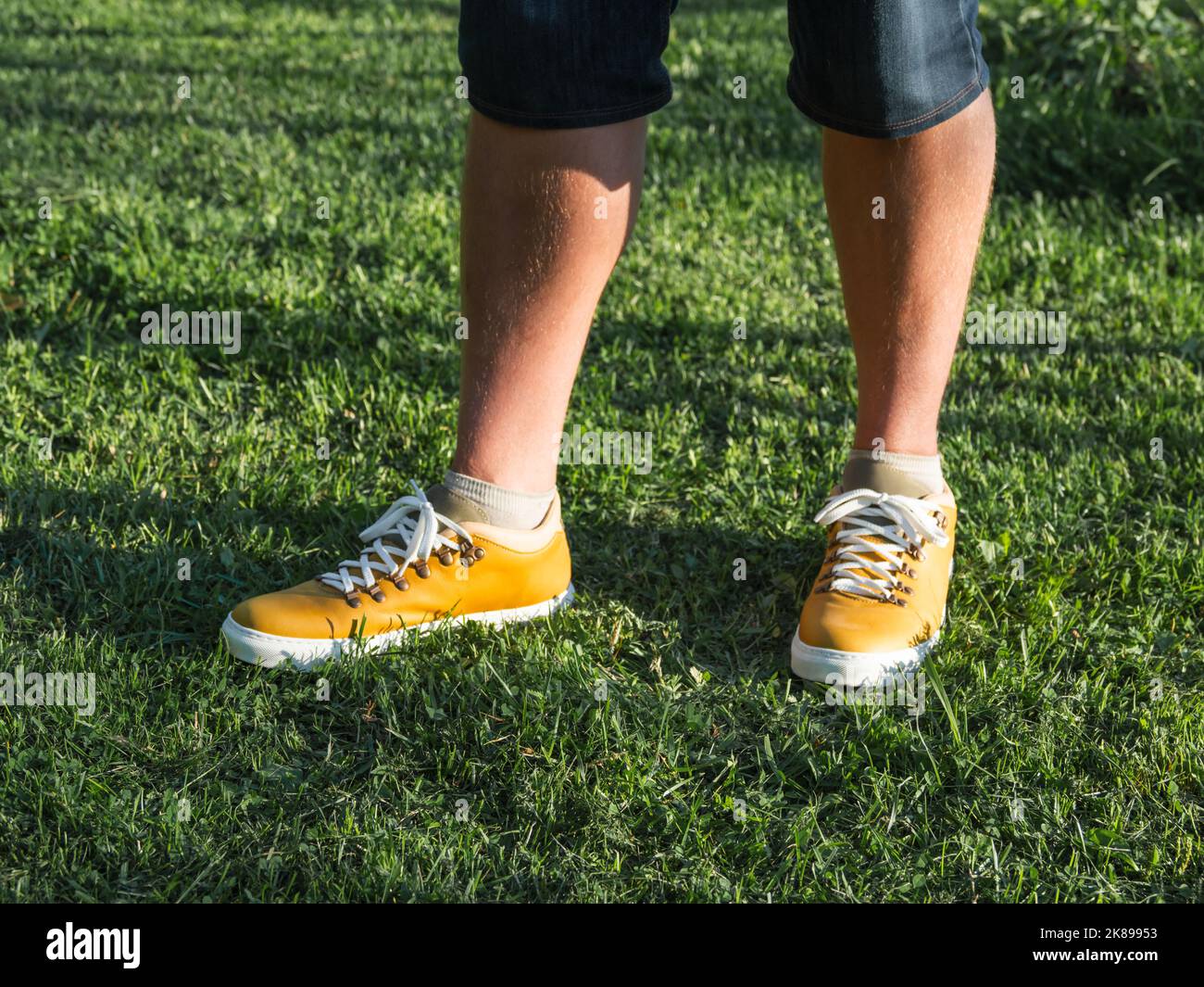 Uomo in sneakers giallo brillante è in piedi su prato verde erba nel parco. Scarpe da hipster moderne. Moda urbana. Foto Stock