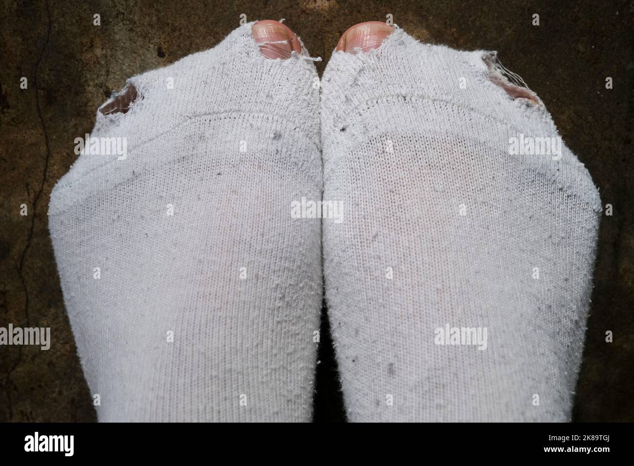 Le dita dell'uomo che attraversano i fori nei calzini bianchi, concetto di hardship Foto Stock