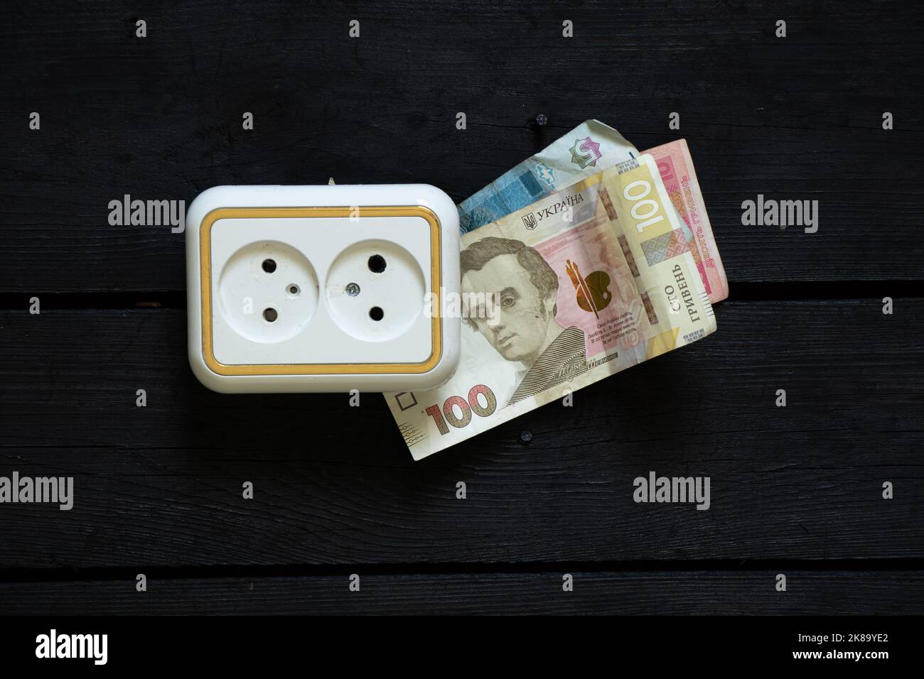 la plastica razetkana su un vecchio muro di legno e vicino a 100 hryvnia, aumento dei prezzi dell'elettricità, dei prezzi dell'elettricità, un altro aumento dei prezzi Foto Stock
