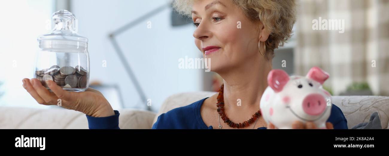 Donna anziana tenere contenitore di vetro con soldi risparmiati per la pensione e piggybank Foto Stock