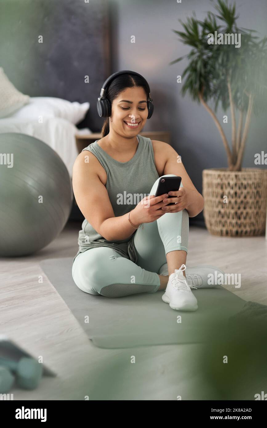 Ho iniziato a ordinare la musica prima di iniziare. Una giovane donna sportiva che indossa le cuffie e usa un cellulare mentre si allenava a casa. Foto Stock