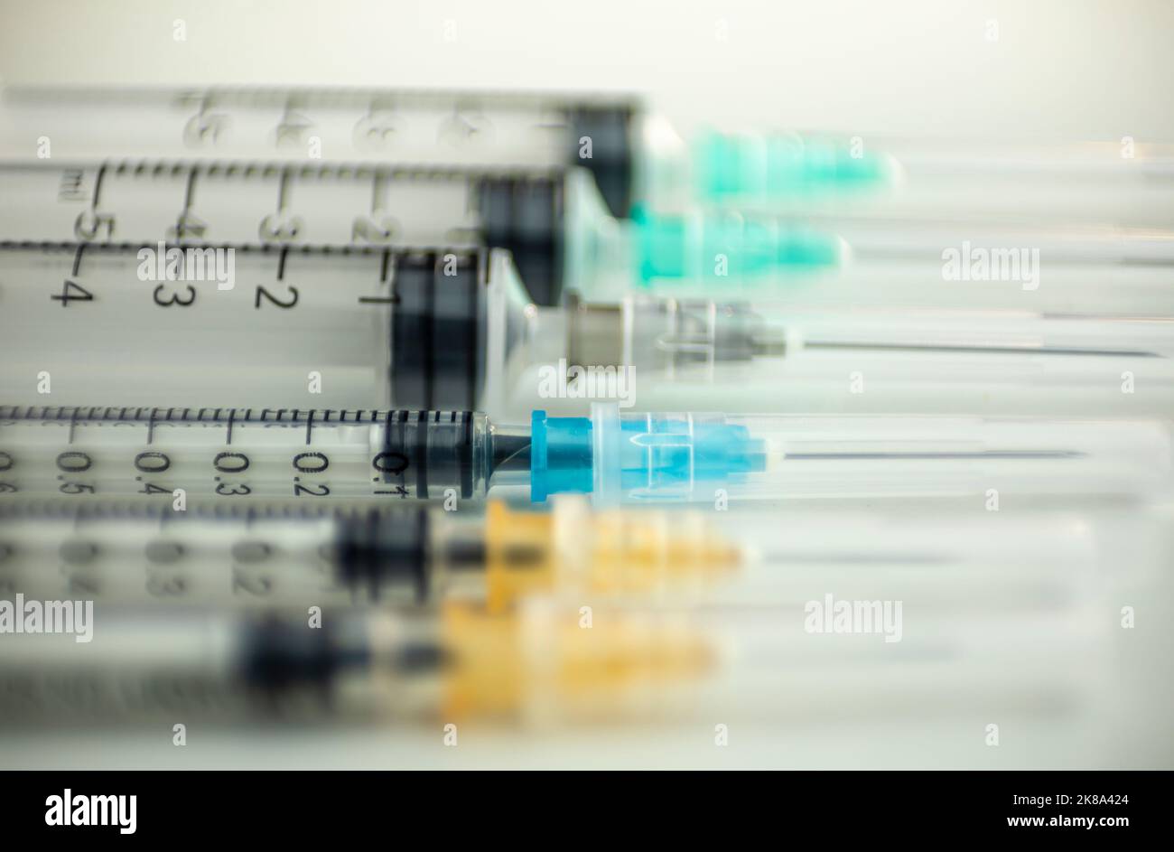 Sei siringhe di diversi spessori e colori su un tavolo bianco ben illuminato Foto Stock