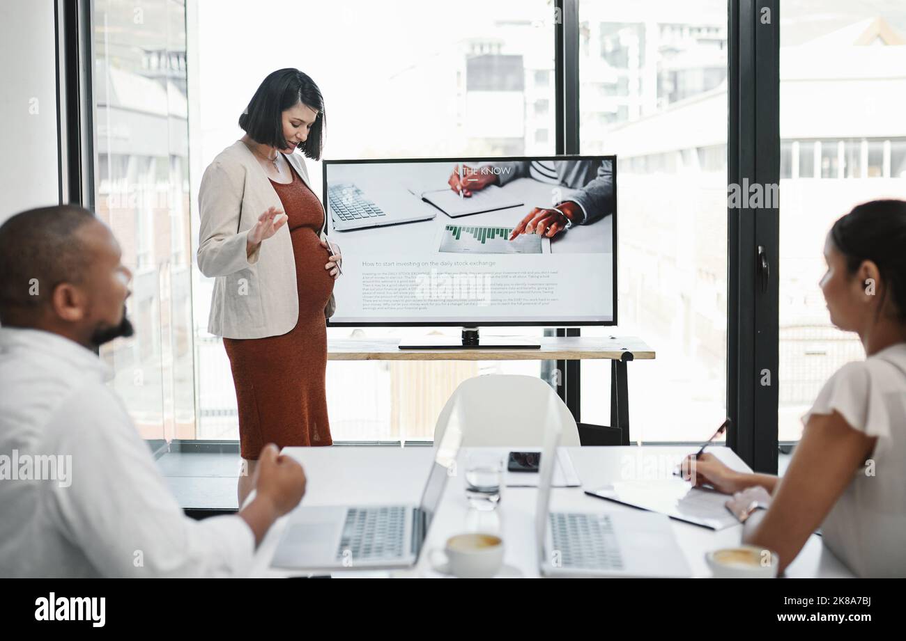 Prendiamo una pausa per le calci a farfalla. Una giovane donna d'affari incinta che consegna una presentazione al suo team in un ufficio moderno. Foto Stock
