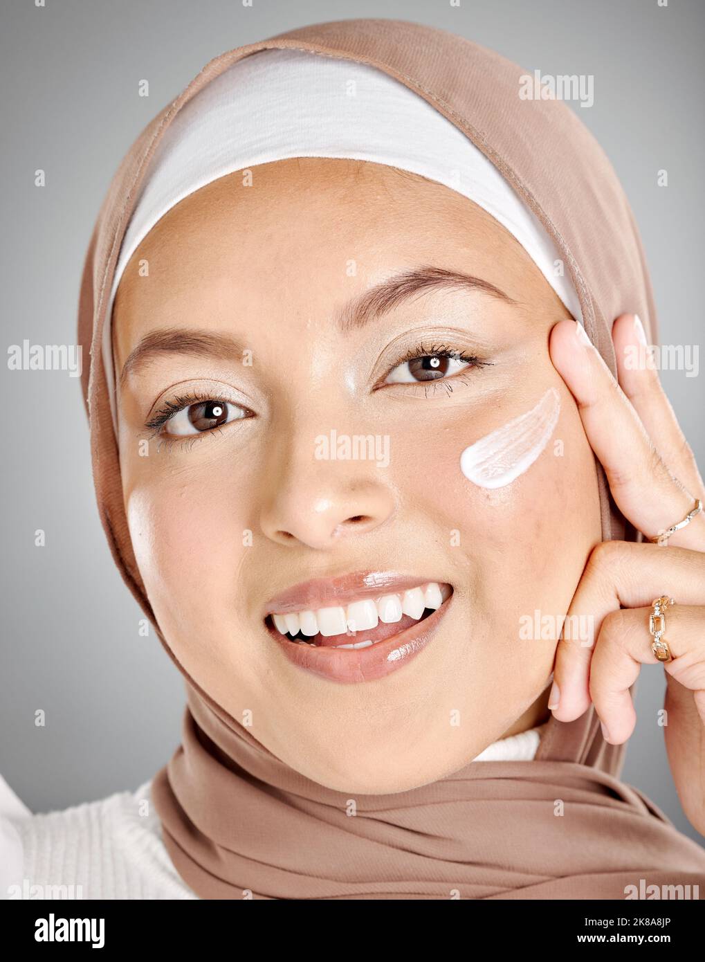 Crema per la cura della pelle, hijab e donna musulmana con un sorriso utilizzando lozione di bellezza e idratante per la pelle. Ritratto di un volto felice di una persona dall'Iran utilizzando un Foto Stock