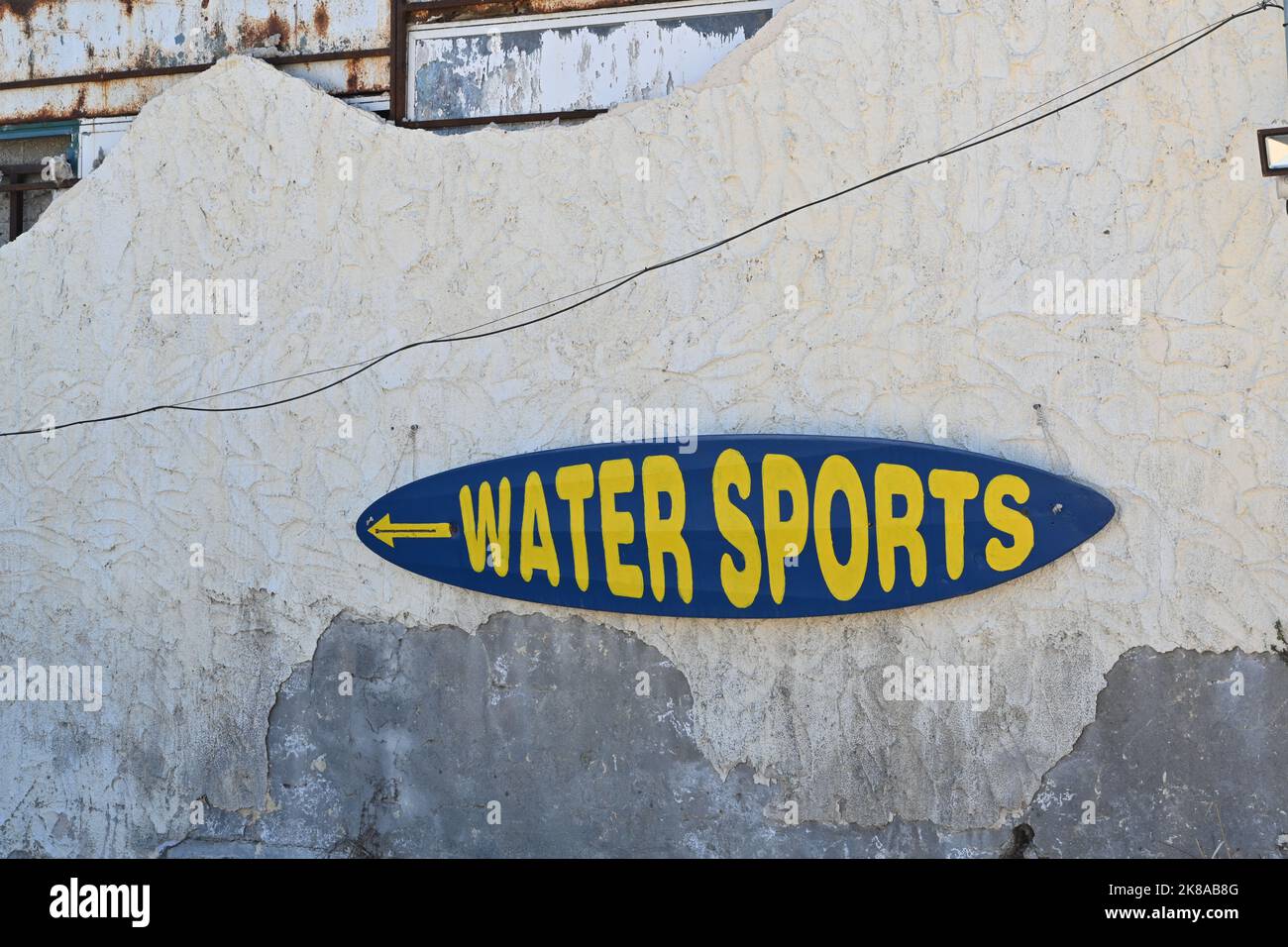 Scudo ovale blu con lettere e parole gialle, sport acquatici, è attaccato alla vecchia parete danneggiata e incrinata. Foto Stock