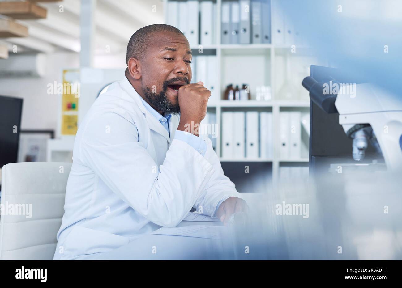 Troppa scienza, non abbastanza sonno. Uno scienziato che guarda stanco mentre conduce la ricerca in un laboratorio. Foto Stock