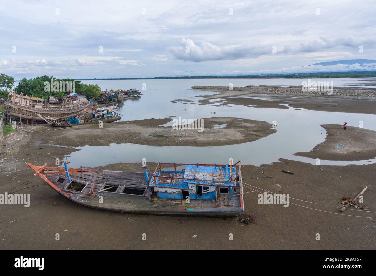 Aceh, Indonesia. 22 ottobre 2022. Un cantiere particolare per i pescherecci nella zona estuario del villaggio di Pusong, Lhokseumawe City. Le tradizionali barche da pesca vengono costruite utilizzando il legno come materiale primario. Non c'è attività dei lavoratori, sono fuori nei fine settimana. Due barche danneggiate devono essere riparate e ormeggiate nella sabbia con funi interbloccanti. Foto Stock