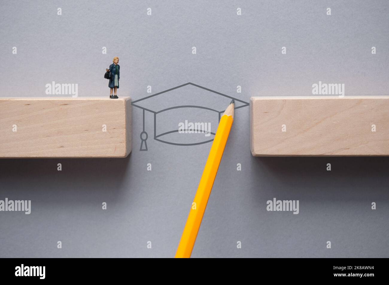 Disegno a matita con cappello graduato che colma lo spazio tra i blocchi di legno per la figura in miniatura femmina da incrociare Foto Stock