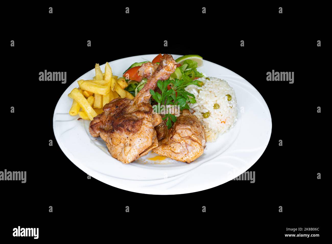 Costolette di pollo grigliate con riso, insalata e patatine fritte in un piatto bianco su sfondo nero Foto Stock