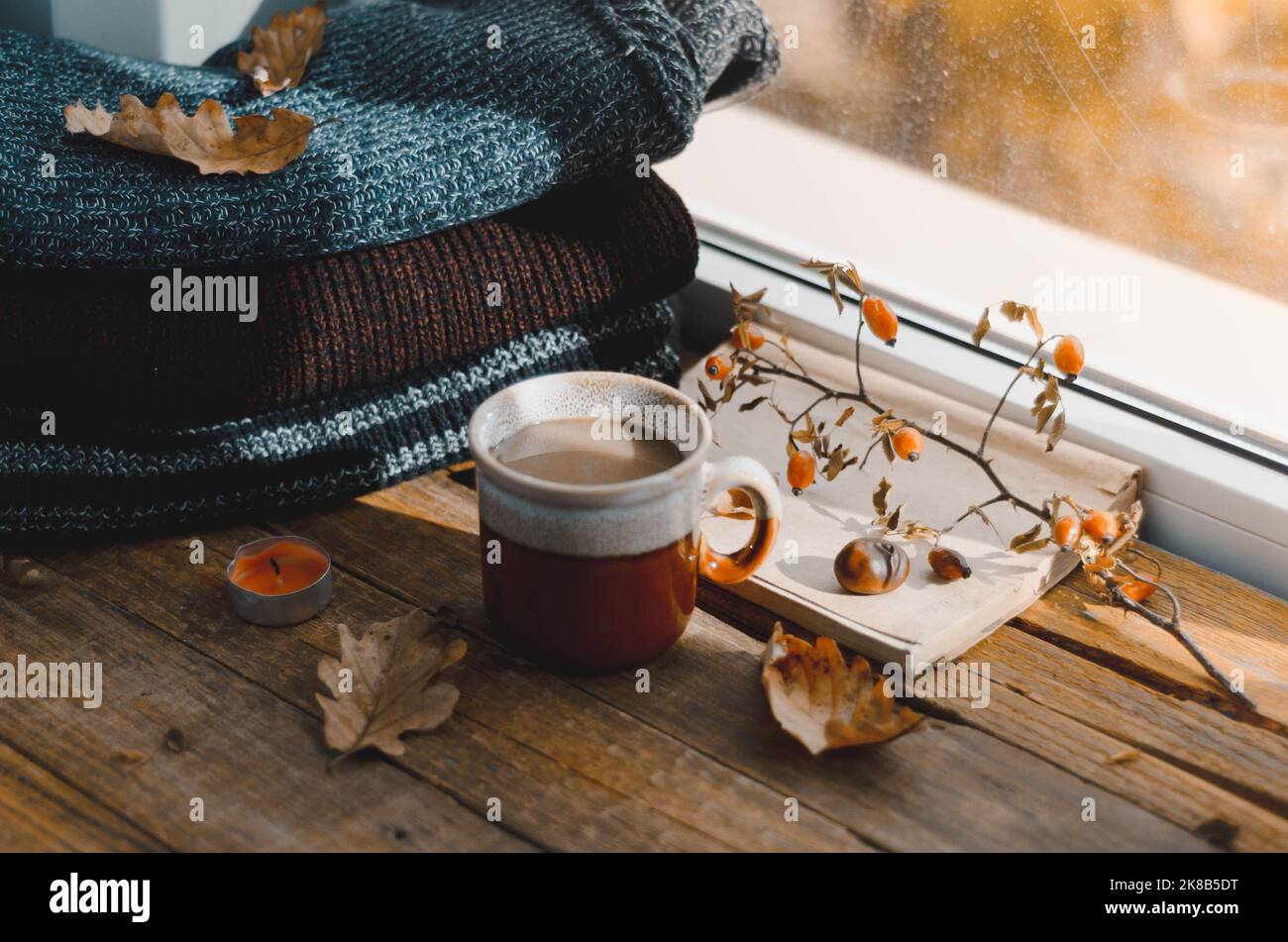 Tazza grande di cappuccino su sfondo marrone vintage. Autunno, foglie autunnali, tazza di caffè calda e fumante e una sciarpa calda su sfondo tavolo di legno. Mari Foto Stock