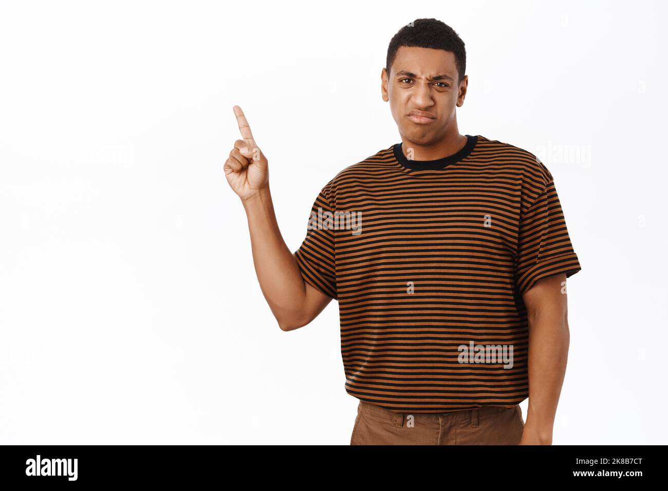 Uomo afroamericano rovesciato che indica il testo di promozione, mostrando la bandiera con l'espressione di faccia delusa, sfondo bianco Foto Stock